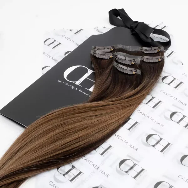 Cascata Hair Extensions - Salted Caramel Brownie Full Set - Image of brunette hair extensions sitting on Cascata branded wrapping paper which is white with black Cascata logos repeated across it
