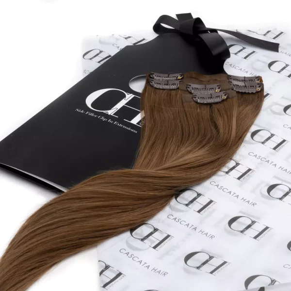 Cascata Hair Extensions - Toffee Brunette Full Set - Image of brunette hair extensions sitting on Cascata Branded Wrapping Paper, which is white, with Black Cascata logos repeated on it.