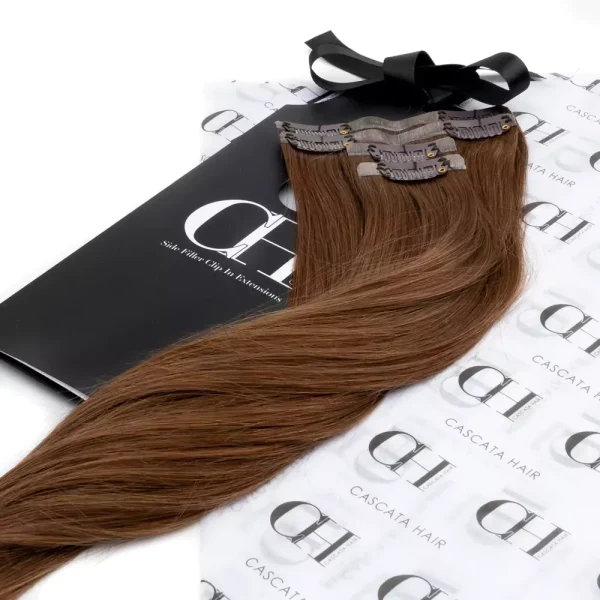 Cascata Hair Extensions - Warm Espresso Side Fillers - Image of hair extensions sitting on Cascata Branded Wrapping Paper, which is white, with Black Cascata logos repeated on it.