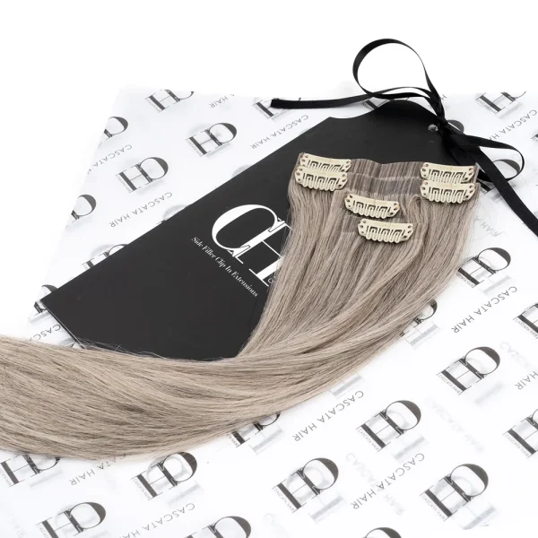 Cascata Hair Extensions - Arctic Fox Side Fillers - Image of blonde hair extensions sitting on Cascata Branded Wrapping Paper, which is white, with Black Cascata logos repeated on it.